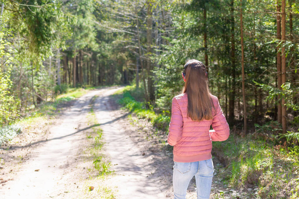 jeden piękny wesoły szczupły pasuje cienki nastolatek dziewczyna korzystających, słuchając muzyki w lesie podczas spaceru lato, wiosna dzień las lub park.Back view. - Zdjęcie, obraz
