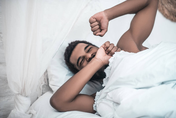 Sleepy yawning darkskinned man in white bed - Fotoğraf, Görsel