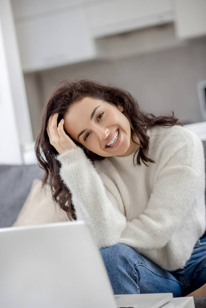 Young woman sitting on the sofa with a laptop and looking happy - 写真・画像