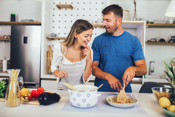 mooi jong paar is praten en glimlachen tijdens het koken gezond eten in de keuken thuis. - Foto, afbeelding