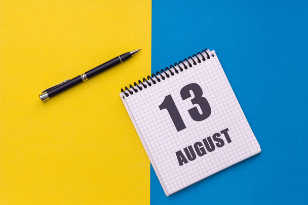 13 de agosto. Día de 14 meses, fecha del calendario. Un cuaderno con una espiral y un bolígrafo se encuentra sobre un fondo amarillo-azul, plano, espacio para copiar - Foto, Imagen
