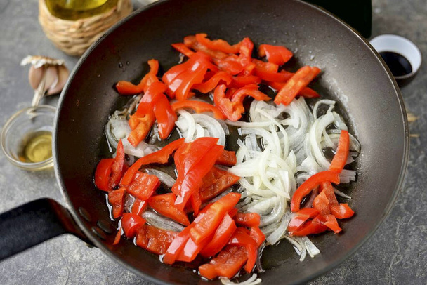 Heat vegetable oil in a frying pan, put onion chopped in half rings and bell pepper into thin strips, fry for a minute. - Foto, Imagen