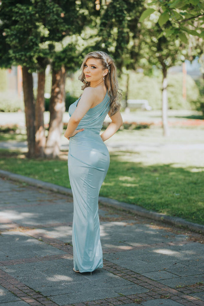 A young and sexy Caucasian female in a long baby blue dress posing in the park - Photo, Image