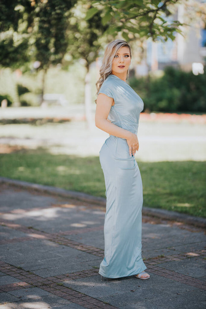 A young and sexy Caucasian female in a long baby blue dress posing in the park - Zdjęcie, obraz