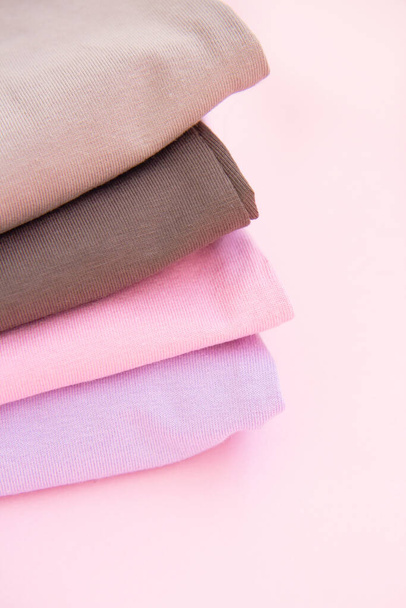 Colorato cotone piegato vestiti stack. Pila di vestiti multicolore su sfondo rosa. Set di vestiti in colori nudi - Foto, immagini
