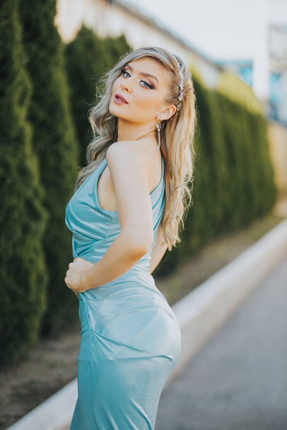 A young and sexy Caucasian female in a long baby blue dress posing in the park - Fotó, kép