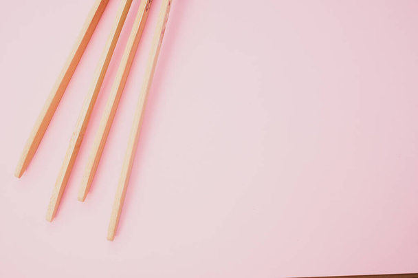 A closeup of two wooden cooking chopsticks on a pink surface - Fotoğraf, Görsel