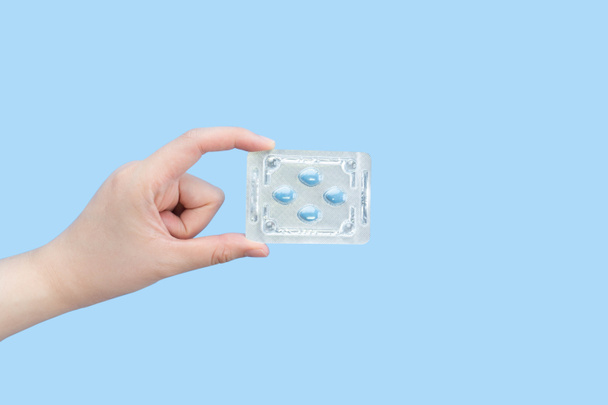 Hands holding sildenafil (Viagra) pills in blister package on blue background. Indication of sildenafil is treatment of erectile dysfunction, pulmonary arterial hypertension. - Photo, Image