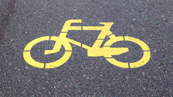 Symbol rowerowy przedstawiający ścieżkę rowerową. Żółty malowany znak dla rowerów na asfalcie. Płaskie ułożenie, widok z góry - Zdjęcie, obraz