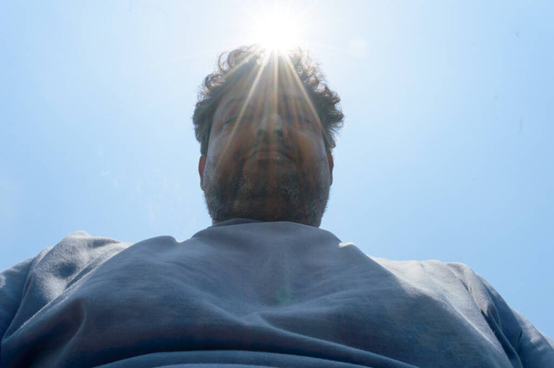 Horké letní sluneční paprsky padají na lidskou hlavu. Člověk se dívá dolů na teplotu slunečního světla. Ochrana před ultrafialovým světlem a spálením pozadí. Úžeh, úpal, skleníkový efekt - Fotografie, Obrázek