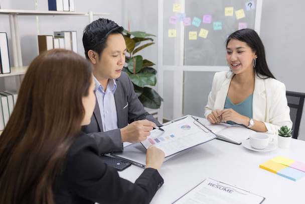 Zmotywowany azjatycki biznesmen w średnim wieku i dwie młode biznesmenki chętnie wymieniały się pomysłami na biznes plany, ciesząc się współpracą w biurze. kierownictwo w miejscu pracy. - Zdjęcie, obraz