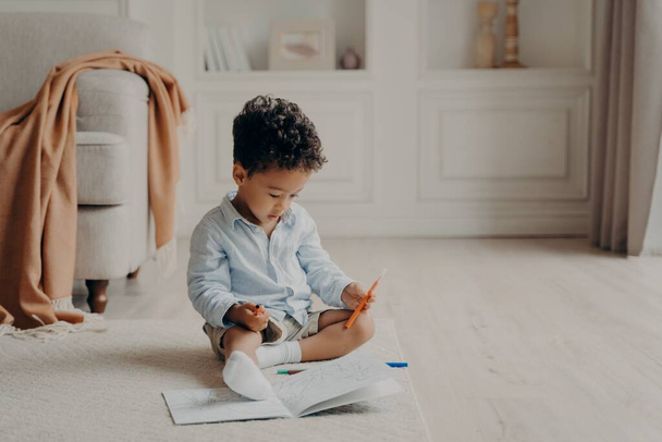 Piccolo riccio afro mulatto ragazzo con libro da colorare a casa - Foto, immagini