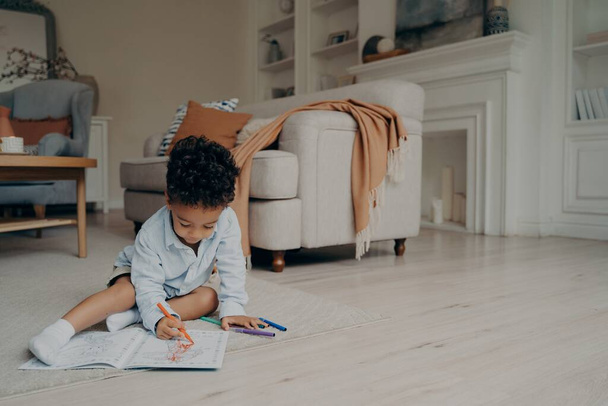 Kleiner Mischlingsjunge zeichnet Malbuch, während er die Freizeit allein zu Hause verbringt - Foto, Bild