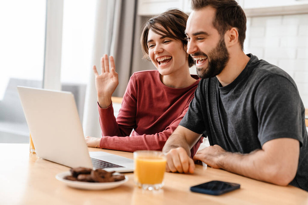 Excited young couple gesturing and using laptop while sitting at home - Фото, зображення