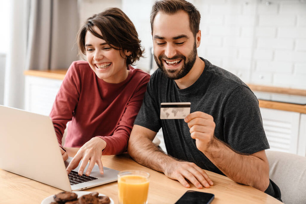 Happy young couple using laptop and credit card while sitting at home - Foto, Bild
