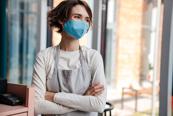 Happy female cafe owner wearing protective face mask, reopening after coronavirus epidemic - 写真・画像