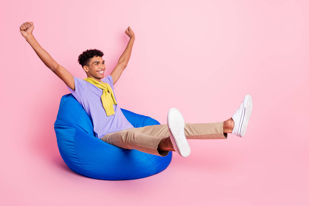Full size photo of young happy cheerful smiling african man sit armchair raise fists in victory isolated on pink color background - Zdjęcie, obraz