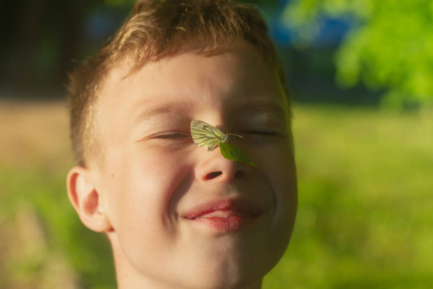 Λευκή πεταλούδα στη μύτη στο πρόσωπο ενός έφηβου αγοριού, το παιδί χαμογελάει και είναι ευτυχισμένο.. - Φωτογραφία, εικόνα