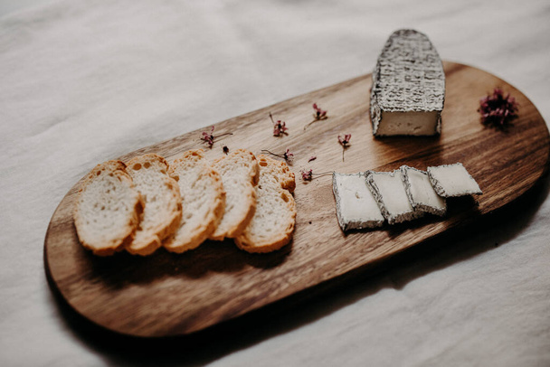 A high angle shot of delicious cheese and slices of bread on a wooden board - Foto, Bild