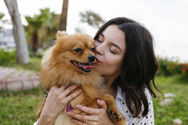 Young woman hugging her pomeranian spitz out in the park. Female bonding with red coated pom dog outside on the walk. Close up, copy space for text, ocean background. - Foto, Bild
