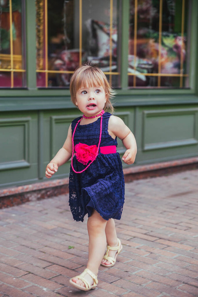 όμορφο κοριτσάκι με φόρεμα τρέχει κάτω από το δρόμο - Φωτογραφία, εικόνα