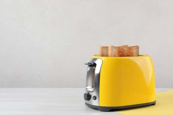 Modern toaster with slices of bread on white wooden table. Space for text - Φωτογραφία, εικόνα