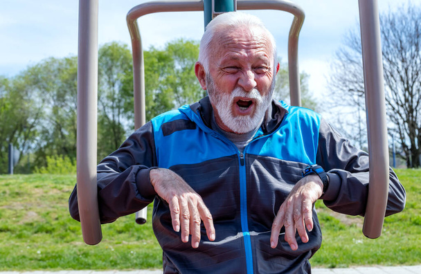Виснажений старший чоловік дихає після тренувань на громадському тренажерному обладнанні під відкритим небом
. - Фото, зображення