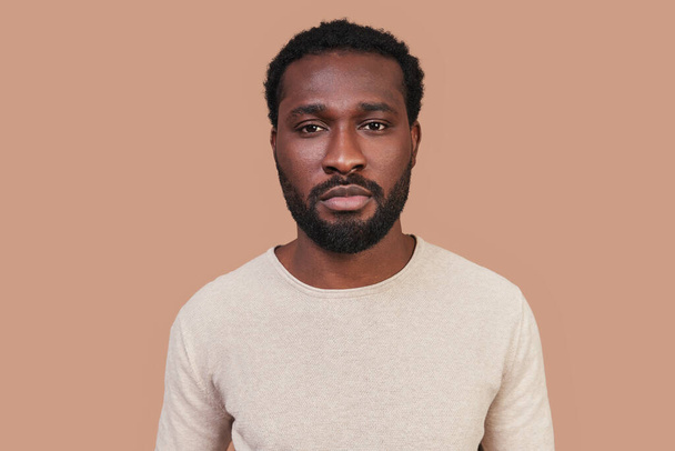 Handsome young African man in casual clothing looking at camera while standing against brown background - Фото, изображение