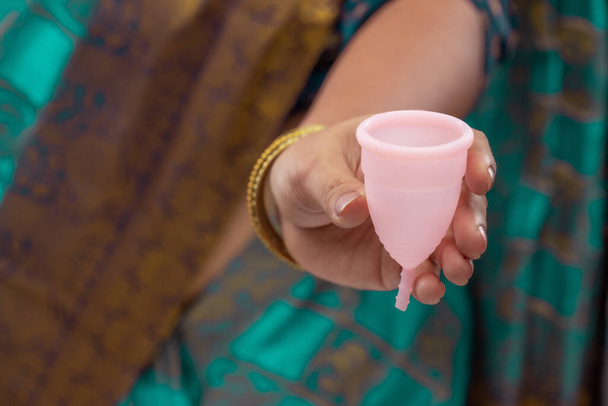 Una mujer india sosteniendo silicio reutilizable Menstrualcup y mostrando diferentes tipos de plegado. - Foto, Imagen