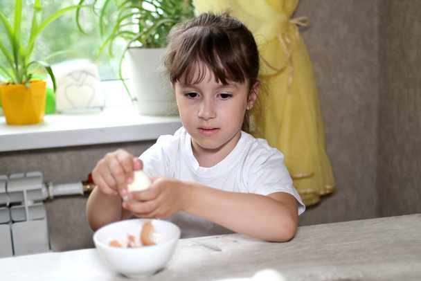 styl życia przedszkolak dziewczynka gotować jedzenie w kuchni. rozwój umiejętności motorycznych w codziennym życiu z materiałów złomowych. dziecko czyści jajka - Zdjęcie, obraz