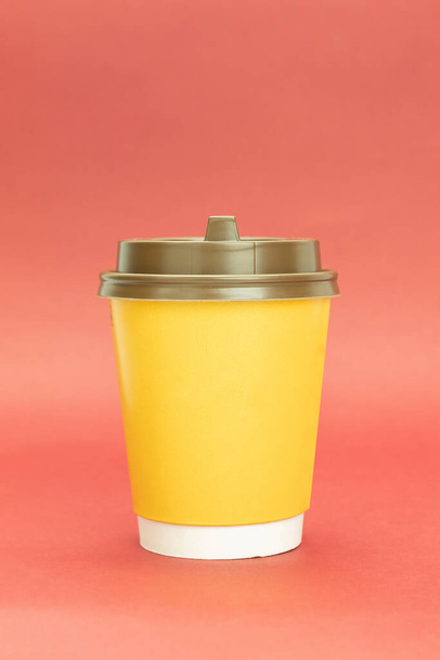 Geel papieren koffiekopje met plastic deksel. Geel glas op een rode achtergrond, met ruimte voor tekst - Foto, afbeelding