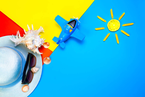 Wakacje i wakacje koncepcji. Akcesoria plażowe muszle, słońce, kapelusz plażowy i płaszczyzna zabawki na kolorowym tle z miejsca na tekst. Widok z góry. Czas letni. - Zdjęcie, obraz