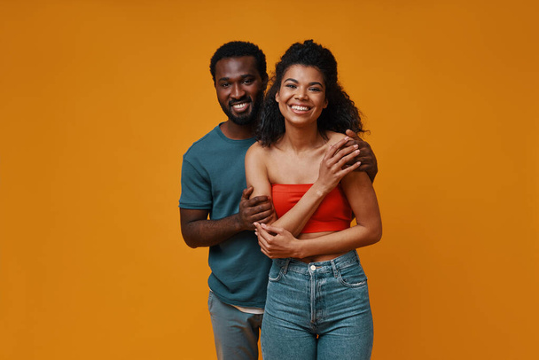 Beautiful young African couple smiling and embracing while standing against yellow background - Valokuva, kuva