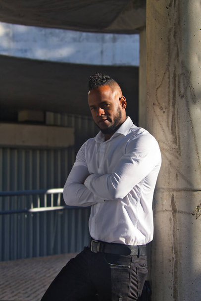 Портрет африканського американця в білій сорочці і чорних штанях, що притулилися до бетонної колонки.. - Фото, зображення