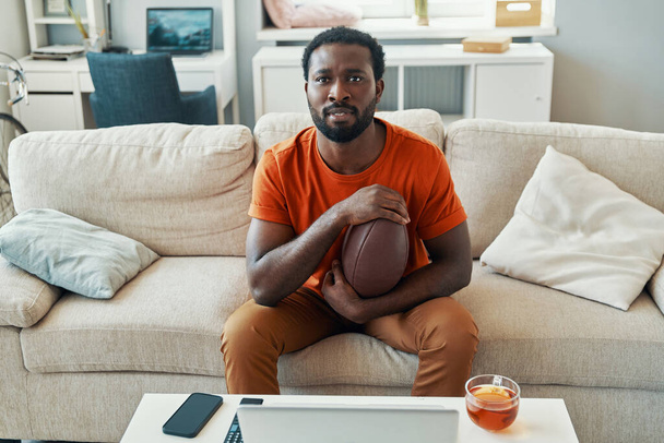 Young African man feeling excited about game while watching sport match at home - 写真・画像
