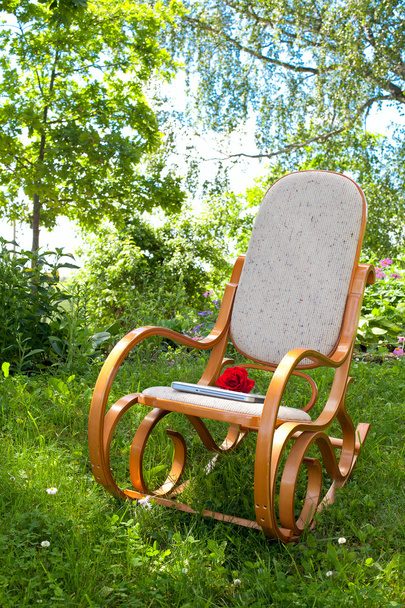 rocking chair with rose and laptop in spring garden - Фото, изображение