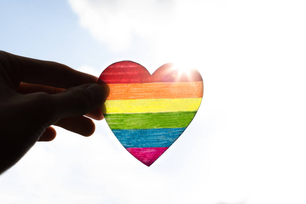 Kalp, yaz gökyüzü ve güneş ışınlarının arka planına lgbtq + renkleriyle boyanmış. LGBTQ + Gurur ayı kavramı - Fotoğraf, Görsel