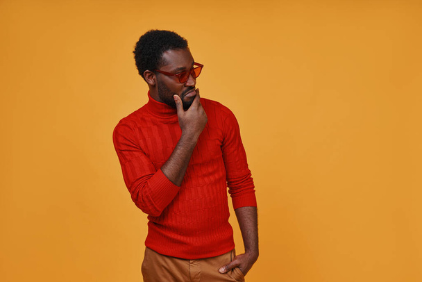 Stylish young African man in eyeglasses looking away while standing against yellow background - Fotoğraf, Görsel