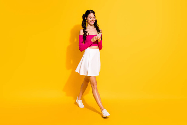 Full size photo of optimistic lovely brunette lady go hold telephone wear pink top skirt isolated on yellow background - 写真・画像
