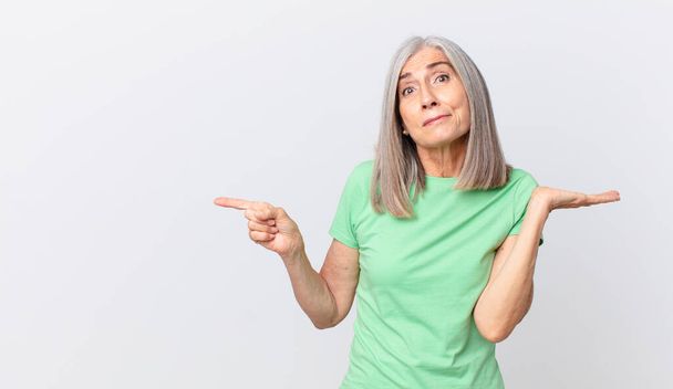 middle age white hair woman feeling puzzled and confused and doubting and pointing to the side - Photo, image