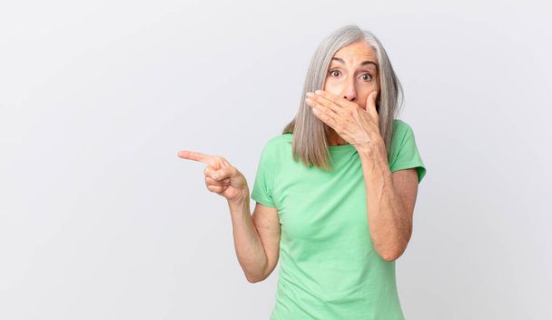 middle age white hair woman covering mouth with hands with a shocked and pointing to the side - Foto, Imagem