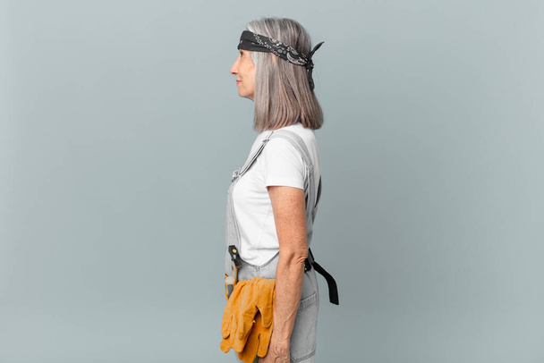 middle age white hair woman on profile view thinking, imagining or daydreaming and wearing work wear and tools. housekeeping concept - Photo, Image