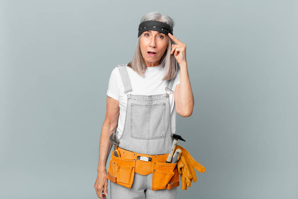 middle age white hair woman looking surprised, realizing a new thought, idea or concept and wearing work wear and tools. housekeeping concept - Fotó, kép