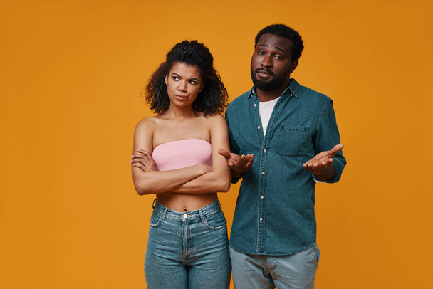 Young African couple gesturing and having a conflict while standing against yellow background - Foto, Imagen