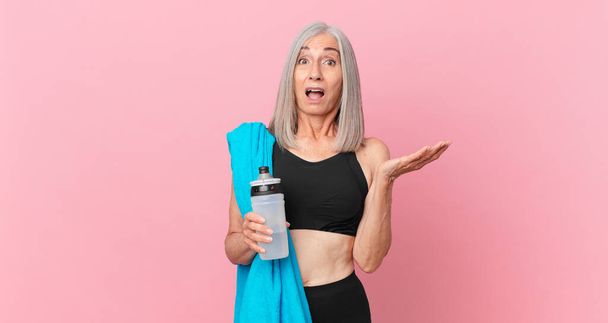 middle age white hair woman amazed, shocked and astonished with an unbelievable surprise with a towel and water bottle. fitness concept - Fotó, kép