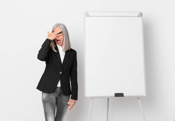middle age white hair woman looking shocked, scared or terrified, covering face with hand and a board copy space. business concept - Foto, Bild