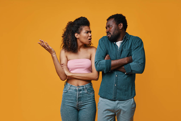 Young African couple gesturing and having conflict while standing against yellow background - Zdjęcie, obraz