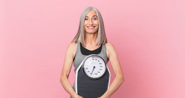 Keski-ikäinen valkoiset hiukset nainen pitelee paino mittakaavassa. kunto ja ruokavalio käsite - Valokuva, kuva