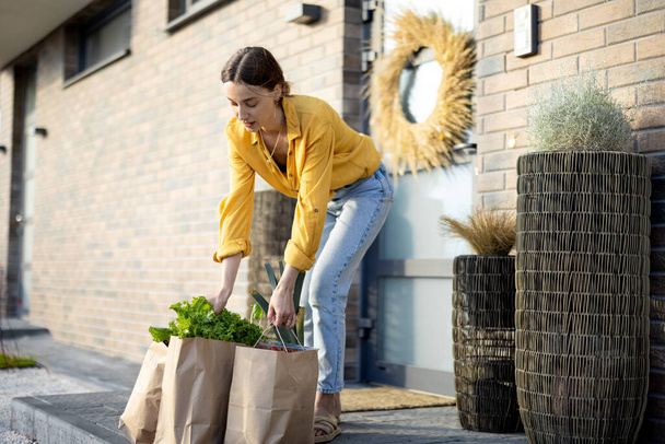 Ama de casa recibiendo comestibles comprados en línea en el porche de su casa - Foto, Imagen