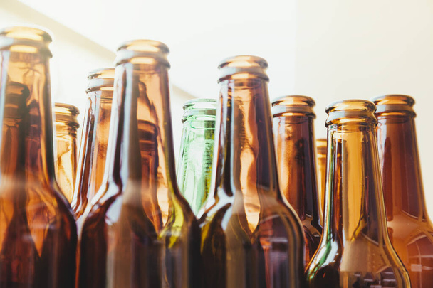 Een lege groene glazen fles omgeven door andere bruine flessen gezien vanuit een lage hoek. Achter de flessen komt veel licht binnen. - Foto, afbeelding